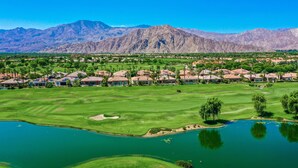 Un parcours de golf avec un lac, entouré de bâtiments résidentiels et avec des montagnes en arrière-plan.
