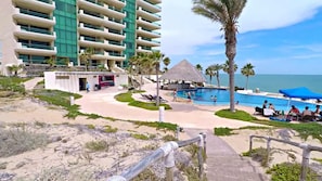 A hotel with multiple floors, a pool area with umbrellas, and a beach view.