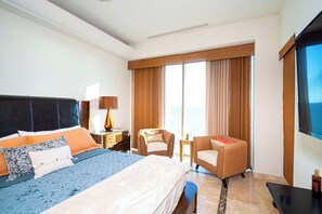 A hotel room with a bed, two armchairs, a small table, a TV, and a large window with curtains. - Tessoro #1002 at Las Conchas – Elevated Luxury on the Sea of Cortez (Puerto Peñasco)