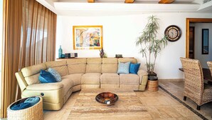 A living room with a sectional sofa, a coffee table, a potted plant, and a clock on the wall. - Beachfront Luxury at Tessoro | 3BR Sleeps 8 | Pool (Puerto Peñasco)