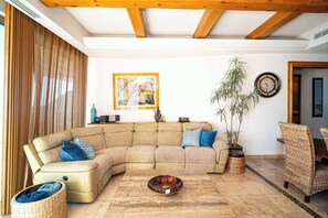 Ein Wohnzimmer mit Ecksofa, Couchtisch, Topfpflanze und einer Uhr an der Wand.