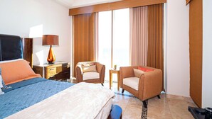 A hotel room with a bed, two armchairs, a desk with a lamp, and a large window with curtains. - Beachfront Luxury at Tessoro | 3BR Sleeps 8 | Pool (Puerto Peñasco)
