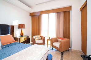 A hotel room with a bed, two armchairs, a desk with a lamp, and a large window with curtains. - Beachfront Luxury at Tessoro | 3BR Sleeps 8 | Pool (Puerto Peñasco)