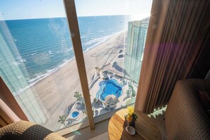 A room with a large window overlooking a beach and a pool area.