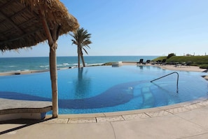 A swimming pool with a view of the ocean, palm trees, and lounge chairs.