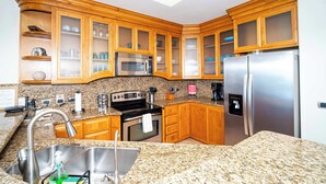 A kitchen with granite countertops, wooden cabinets, stainless steel appliances, and a built-in microwave. - Beachfront Luxury at Tessoro | 3BR Sleeps 8 | Pool (Puerto Peñasco)