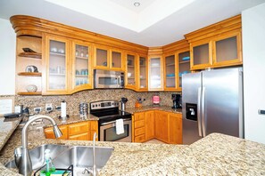 A kitchen with granite countertops, wooden cabinets, stainless steel appliances, and a built-in microwave. - Beachfront Luxury at Tessoro | 3BR Sleeps 8 | Pool (Puerto Peñasco)