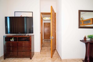 Ein Zimmer mit Fernseher auf einer Holzkassette, einer Holztür, die in einen anderen Raum führt, und einem Spiegel an der Wand.