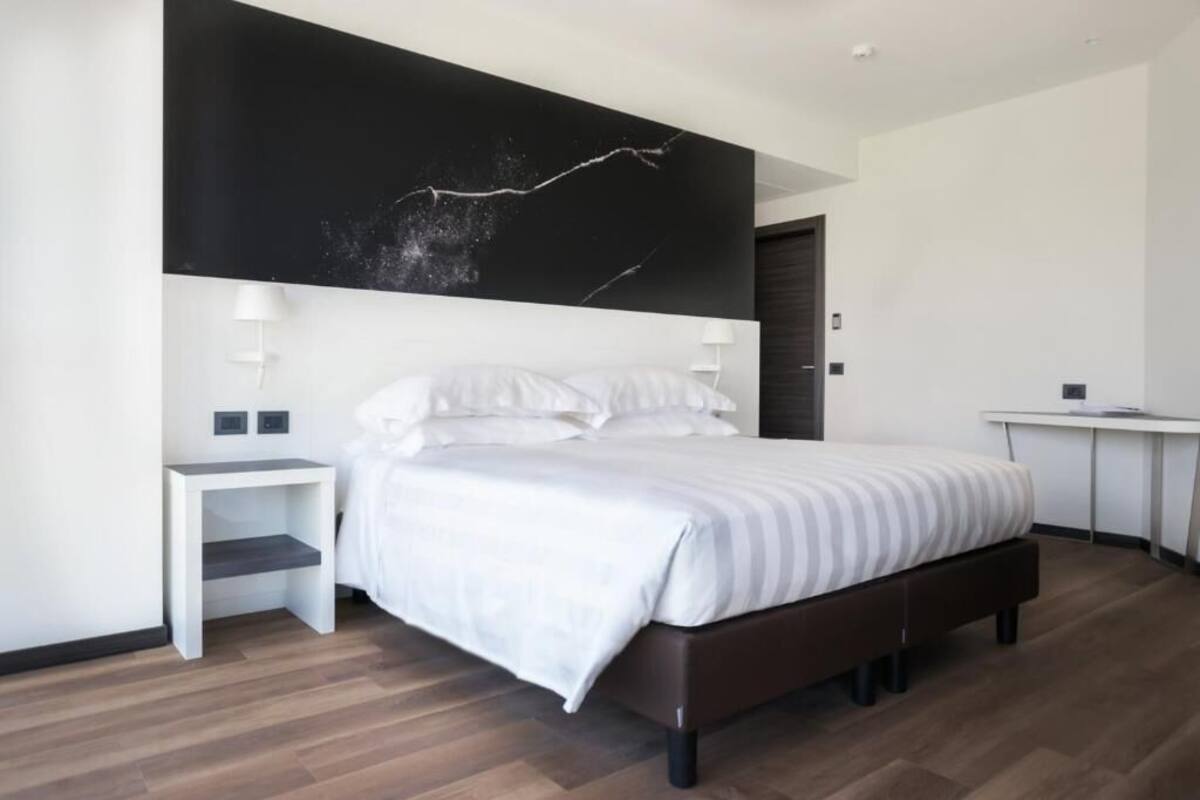 A modern bedroom with a large bed, a white bedside table, a desk, and a black accent wall.