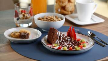 A breakfast setting with a plate of cake, strawberries, and whipped cream, a bowl of cereal, and a glass of orange juice.