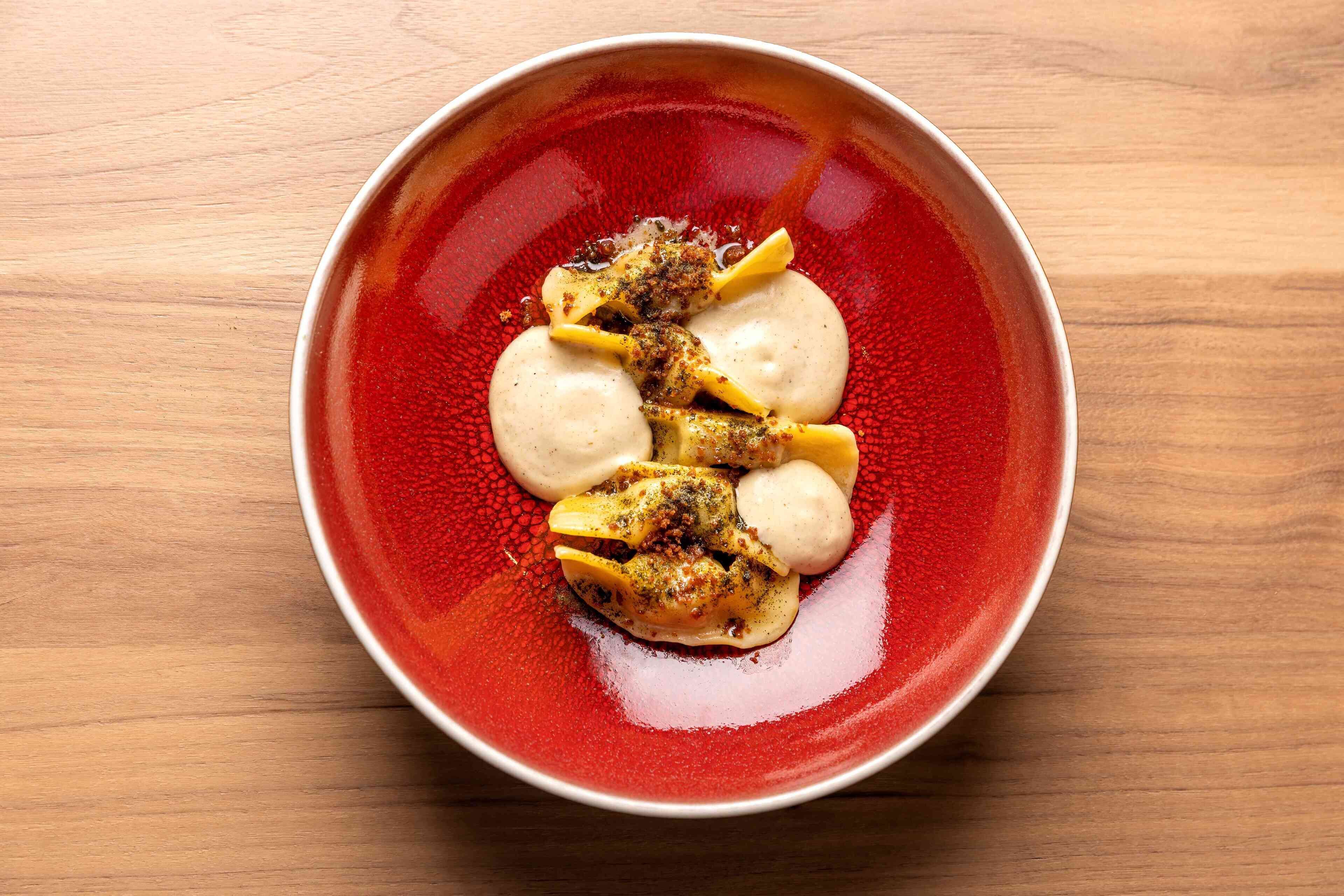 A red bowl with a white rim containing food items on a wooden surface.