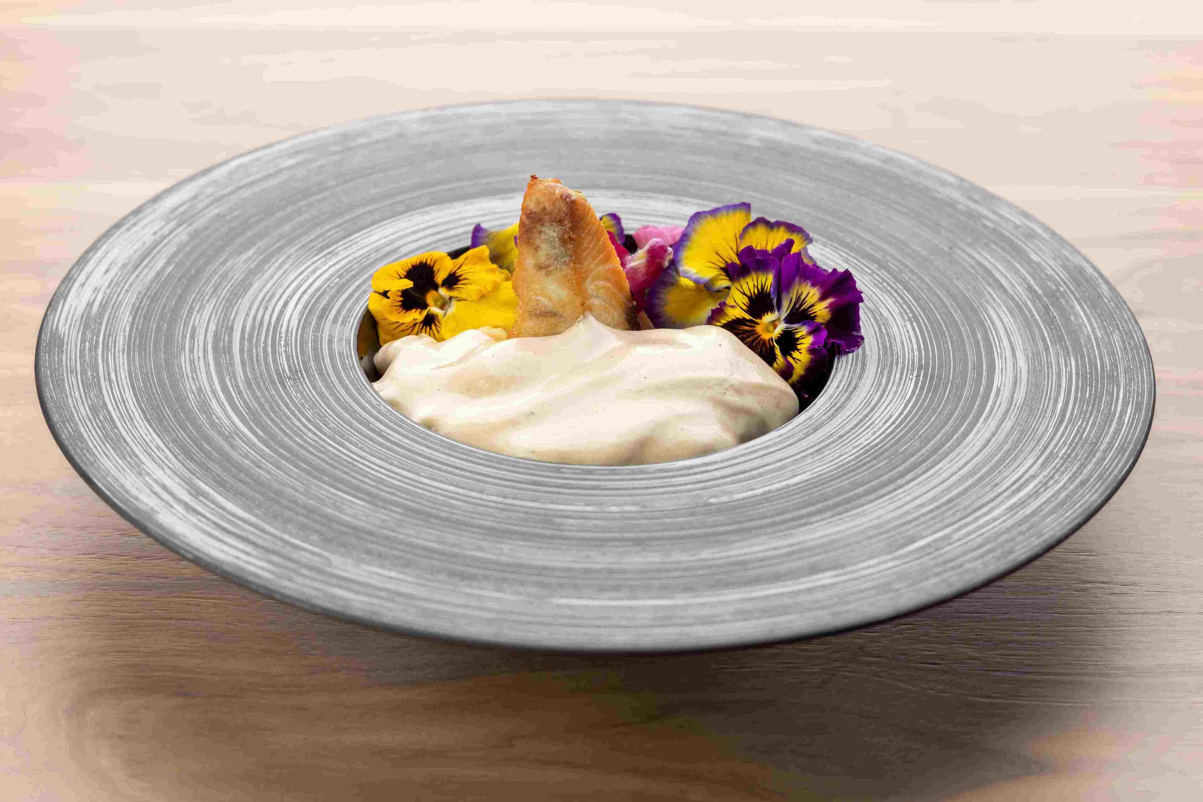 A plate with a creamy dessert, a piece of fried food, and colorful flowers.