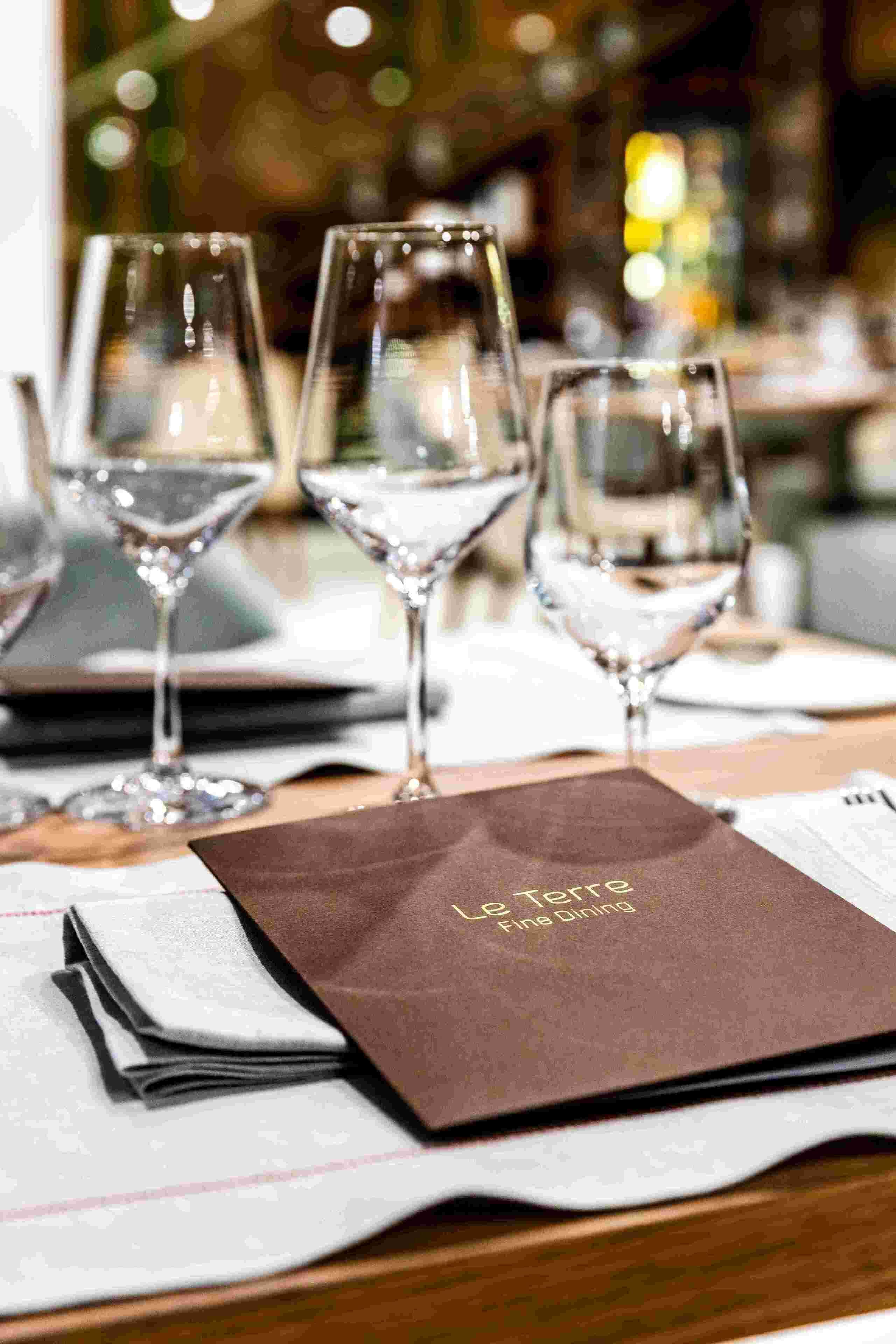 Una mesa dispuesta con copas de vino y un menú en Le Tore Fine Dining.