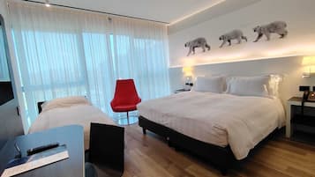 Habitación de hotel con cama, escritorio y una silla, un sillón rojo y un cuadro de osos polares en la pared.
