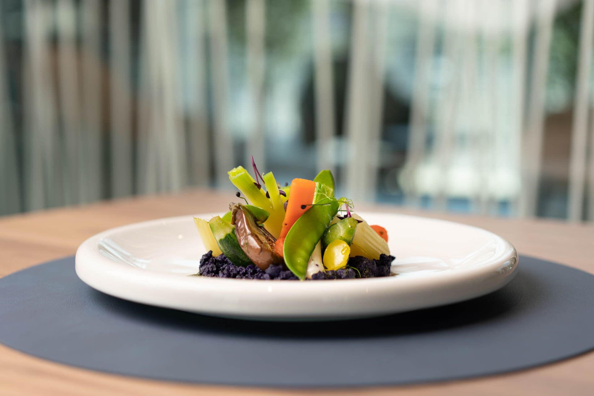 A plate of colorful vegetables on a white plate with a dark mat underneath, set on a wooden table.