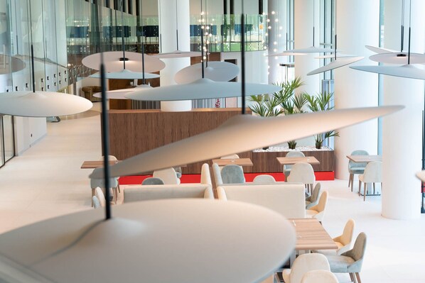A modern interior with round tables and chairs, glass partitions, and a wooden reception desk.