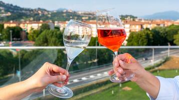 Two hands holding wine glasses with a scenic view of a city and mountains in the background.