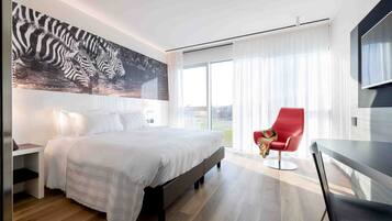 Ein modernes Hotelzimmer mit einem großen Bett, einem roten Sessel, einem Flachbildfernseher und einem großen Fenster mit Vorhängen.