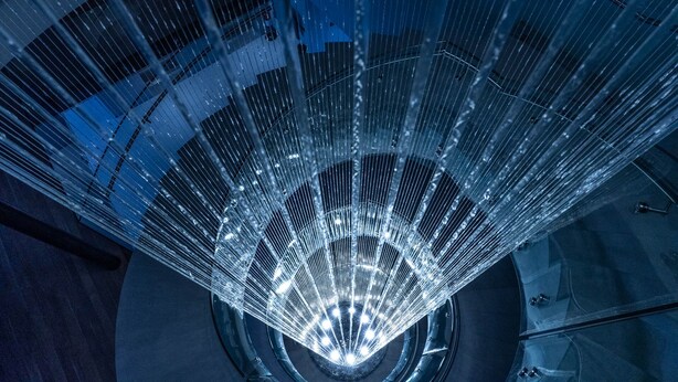 Uma grande estrutura circular de vidro com uma fonte de luz central, rodeada por uma estrutura metálica.