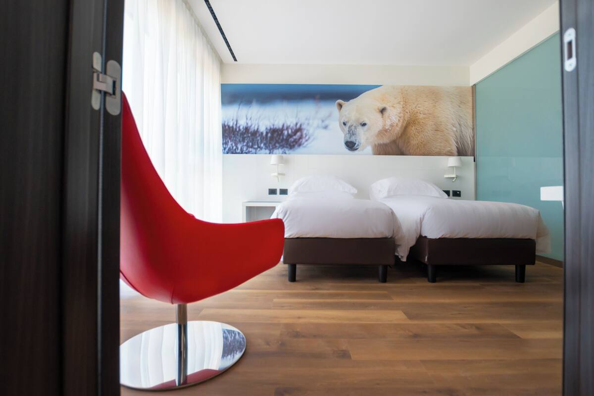 A hotel room with a bed, a red chair, and a large polar bear painting on the wall.