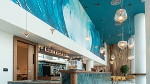 Uma área de bar moderna com um grande mural, prateleiras de madeira com garrafas e um balcão com padrão herringbone.