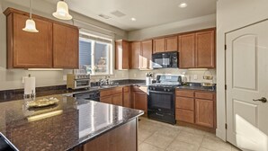 A kitchen with wooden cabinets, a granite countertop, a stove, a microwave, and pendant lights. - Pico in the Pines, pet friendly and cozy fireplace (Flagstaff)