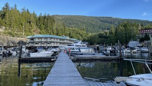 A marina with boats docked, a wooden pier, and a building with a green roof.