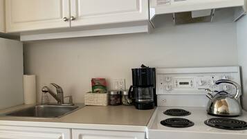 A kitchen with a stove, coffee maker, and a kettle.