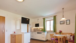Une cuisine compacte équipée d’un four à micro-ondes, d’un évier et de placards. On y trouve également un coin repas avec une table et des chaises, ainsi qu’un lit avec une literie à motifs floraux.
