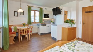 Habitación compacta y bien iluminada con comedor, kitchenette y cama con ropa de cama floral.