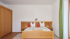 Un dormitorio con una cama de madera, una mesita de noche, una cortina verde y un armario de madera.