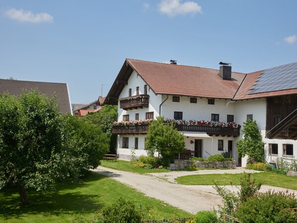 A traditional European-style building with a sloped roof, a balcony with flower boxes, and a gravel path leading to the entrance.
