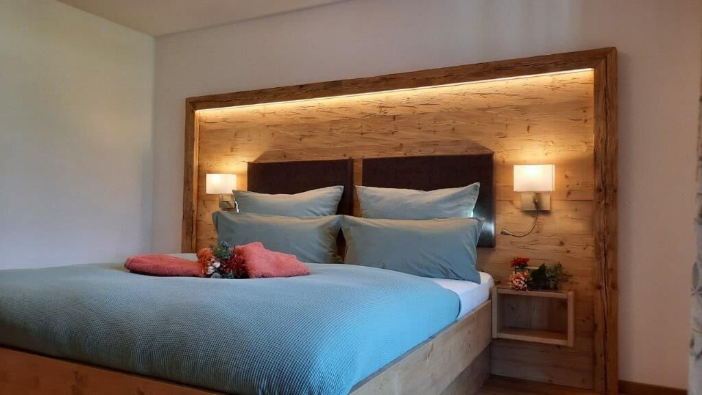 A bed with a wooden headboard, two bedside lamps, and a small bedside table with a flower arrangement.