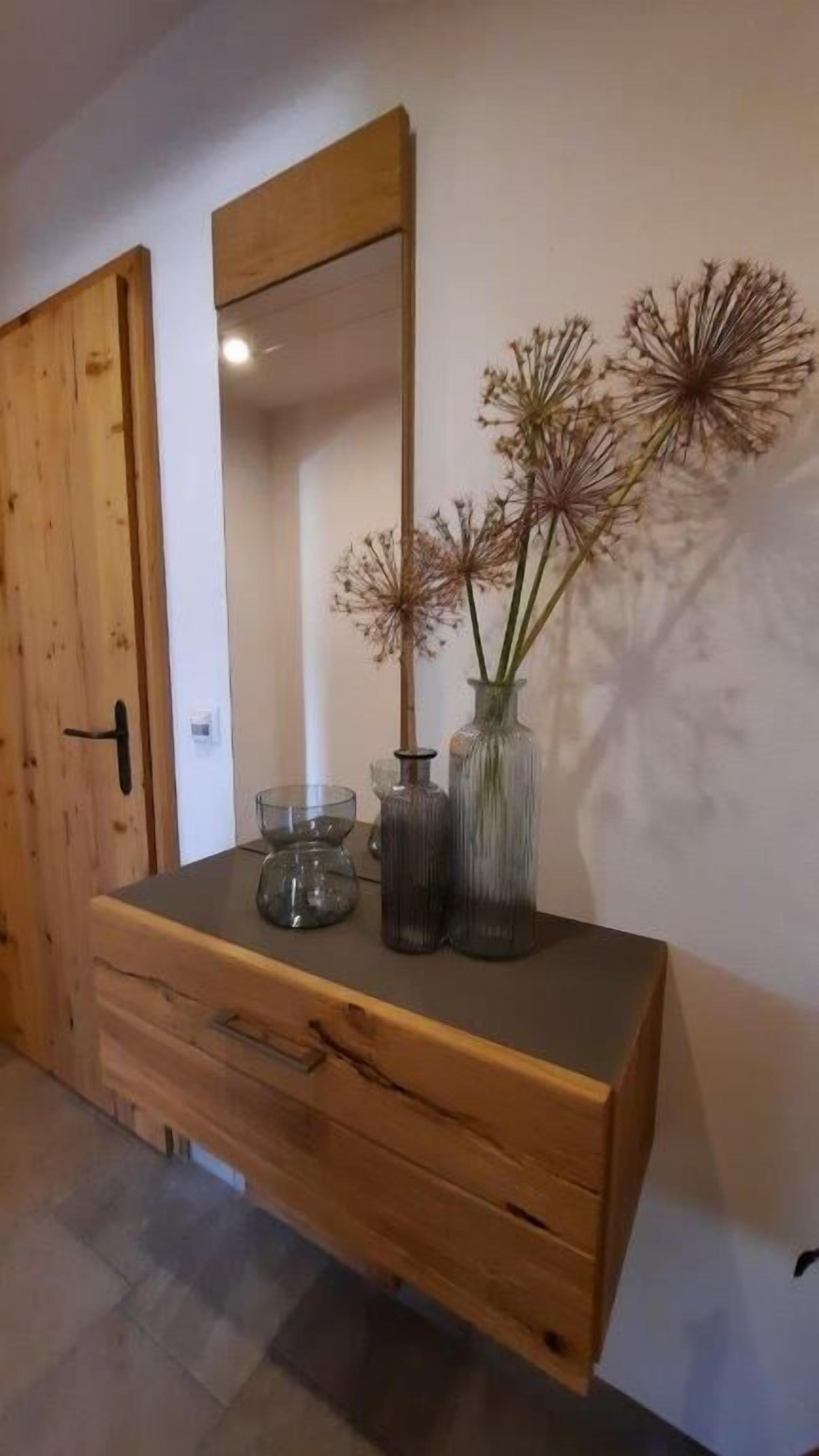 Une commode en bois avec un miroir, un vase contenant des fleurs séchées et un saladier en verre.