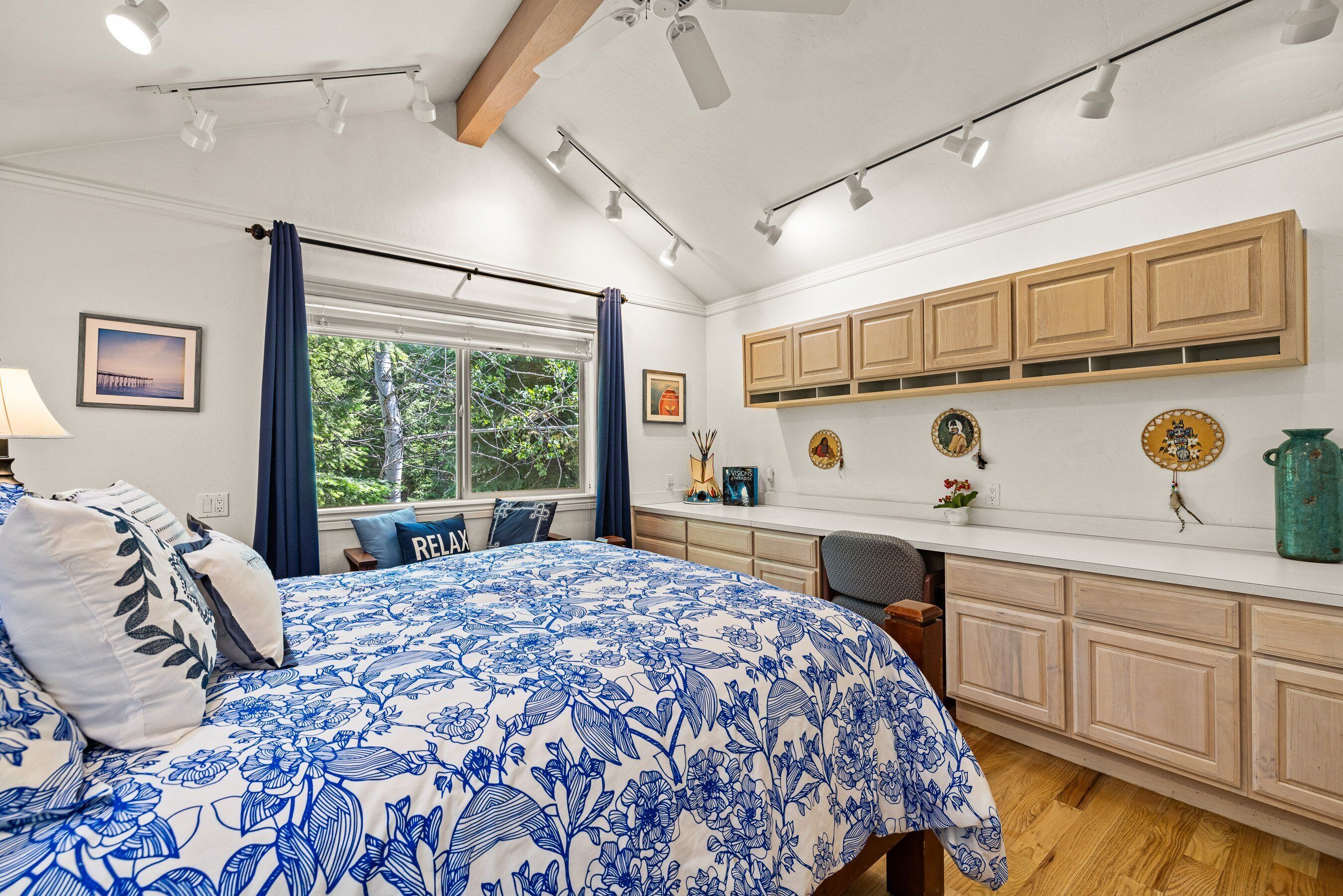 Un dormitorio con una cama grande, una ventana con cortinas, un escritorio y un armario con objetos decorativos.
