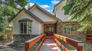 A wooden bridge leading to a house with stone walls and a red door.
