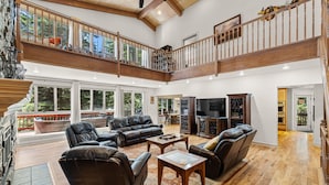 A spacious living area with a high ceiling, wooden flooring, and a balcony with a railing.