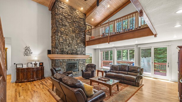 A spacious living room with a stone fireplace, leather sofas, and a high ceiling with exposed beams.