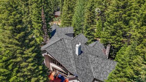 A house with a steeply pitched roof, surrounded by dense forest.