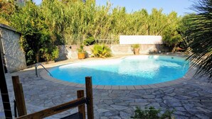 A swimming pool with a stone deck, surrounded by potted plants and a wooden chair. - Rental with swimming pool, close to beaches, at the foot of the maquis. (Biguglia)