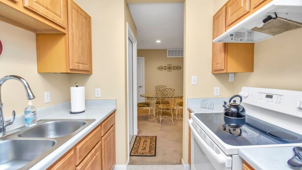 Una cocina con armarios de madera, lavamanos de acero inoxidable, una estufa blanca y una zona de comedor con una mesa y sillas.