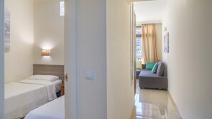A hotel room with two single beds, a nightstand, a wall-mounted lamp, and a view of a living area with a sofa and curtains. - Apartment "Marina Sunny View" with Wi-Fi, Garden & Terrace (Fuengirola)