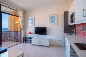 Una cocina moderna con televisión, gabinetes blancos y salpicadero rojo.