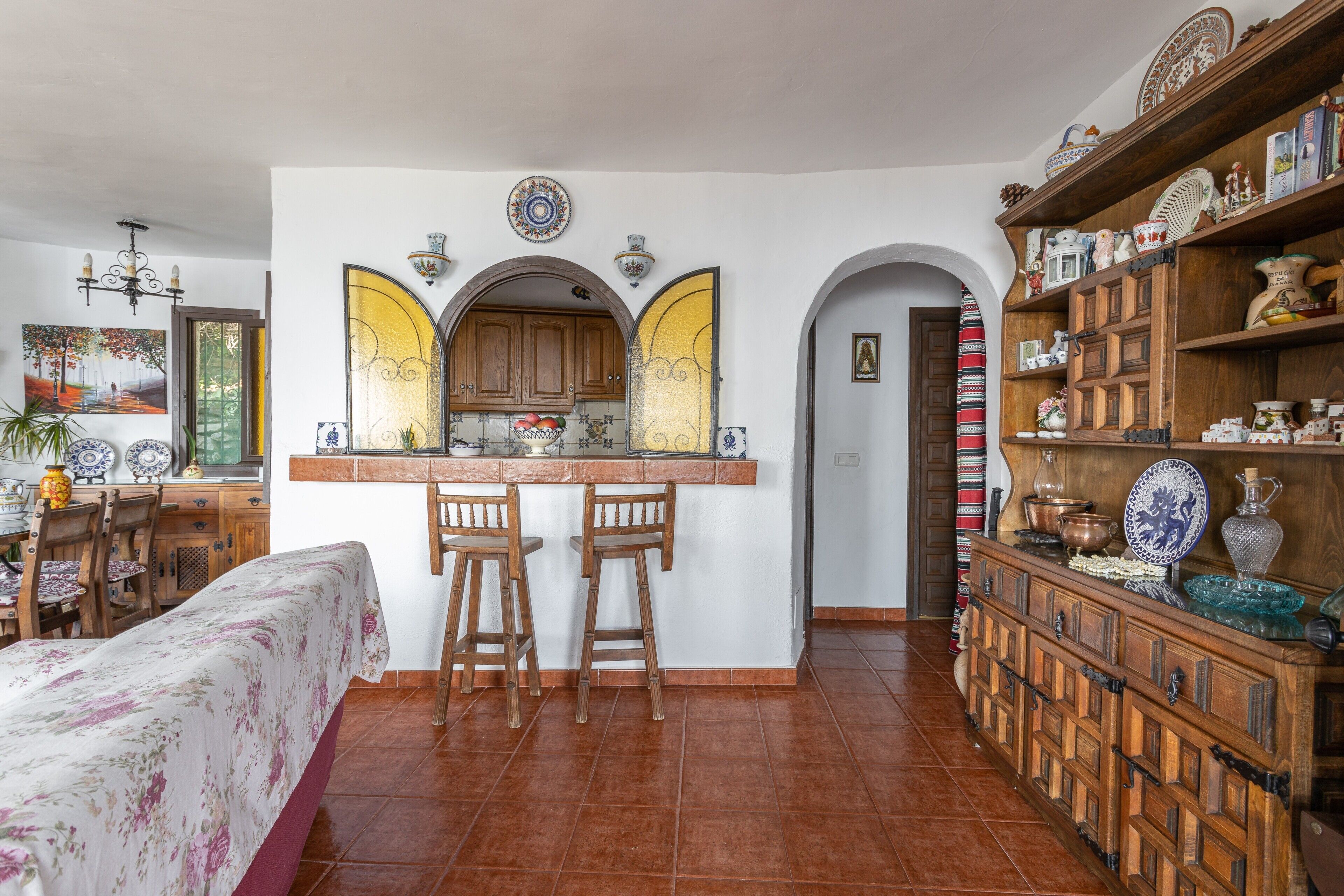 Een keuken met een centraal eiland, houten barstoelen en een decoratieve plank met diverse objecten.