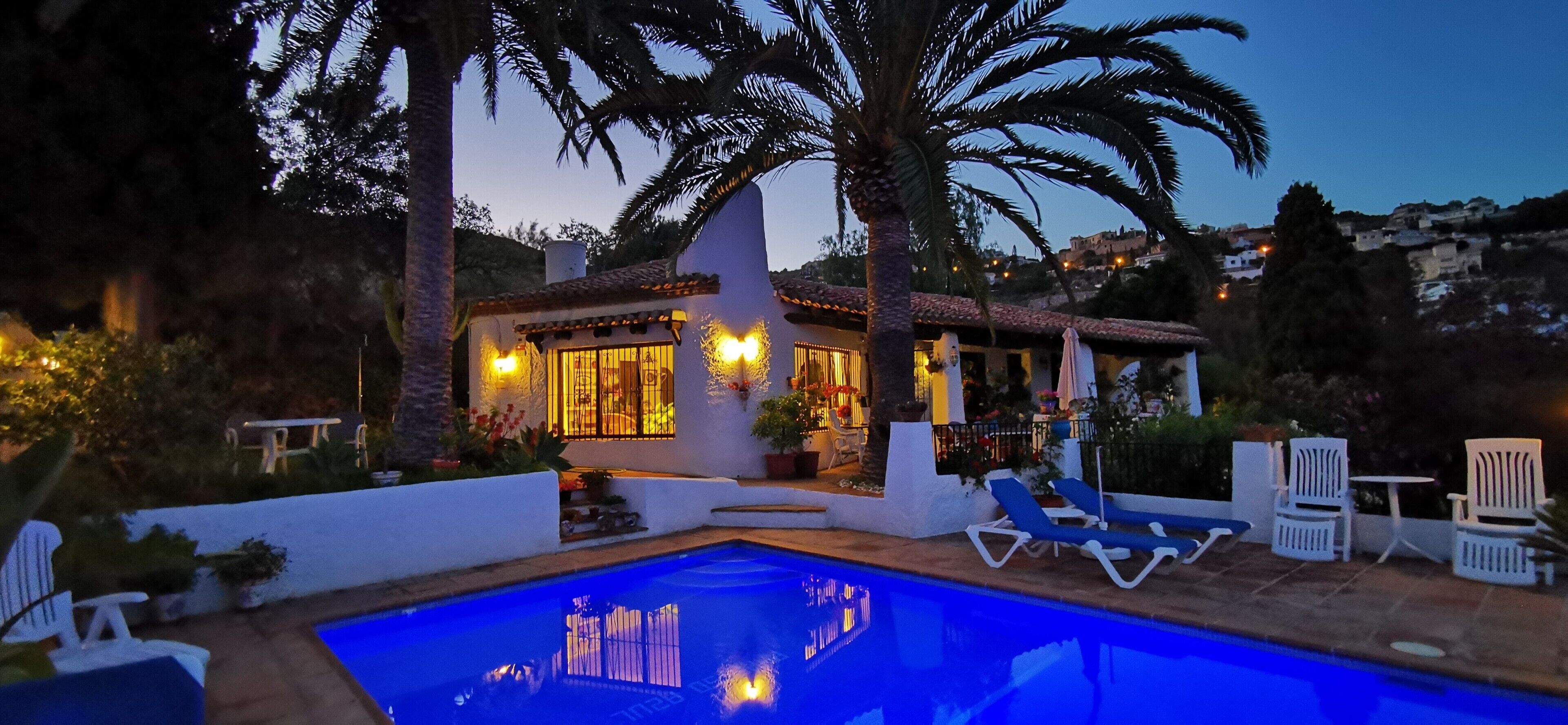 A poolside area with lounge chairs, a pool, and a building with warm lighting.
