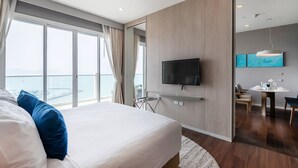 Habitación de hotel moderna con una cama grande, un televisor montado en la pared y vistas al mar a través de las ventanas.