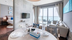 Una habitación de hotel moderna con un ventanal grande, una zona de comedor con una mesa redonda y un rincón de descanso acogedor.