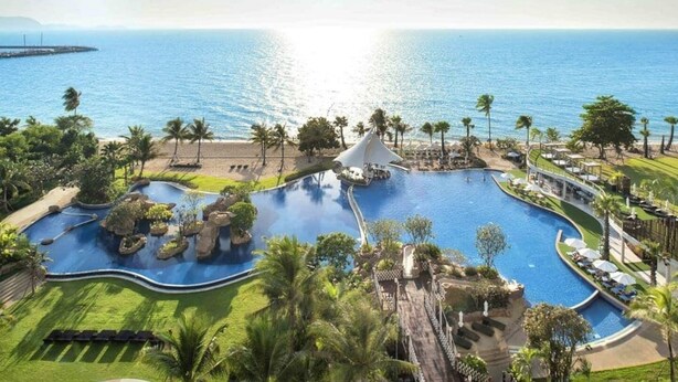 Un resort con una amplia piscina central, palmeras y vistas al océano.