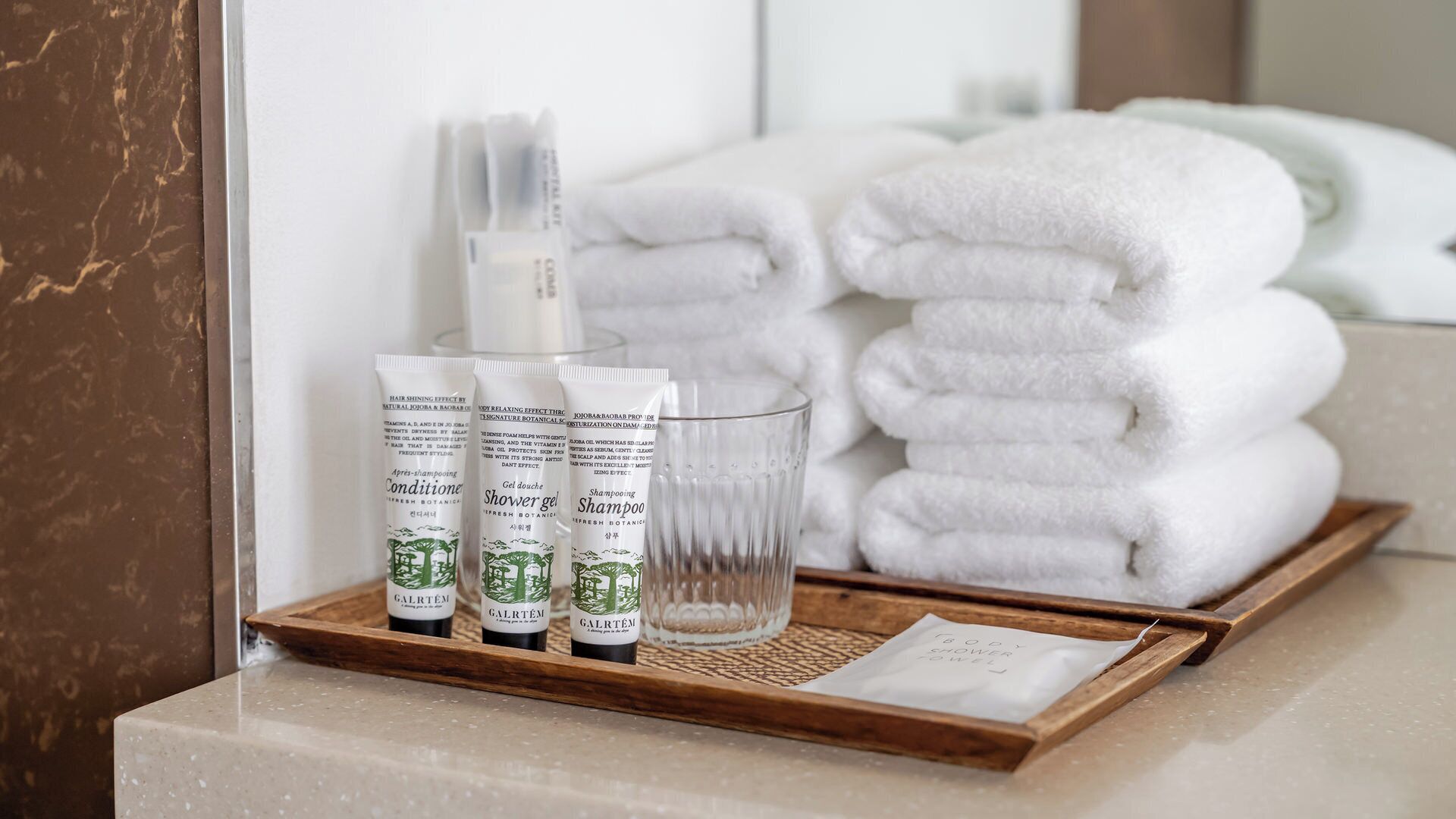 Uma bandeja com produtos de higiene, incluindo gel de banho, shampoo e condicionador, junto com toalhas dobradas com cuidado.