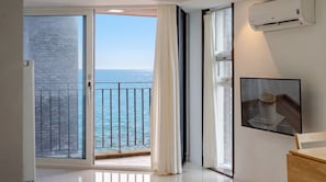 A room with a sliding glass door leading to a balcony with a view of the sea.